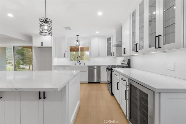 kitchen featuring stainless steel appliances, white cabinetry, beverage cooler, and light stone counters