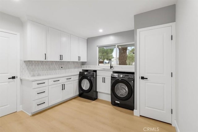 clothes washing area with washer and dryer, cabinets, sink, and light hardwood / wood-style flooring