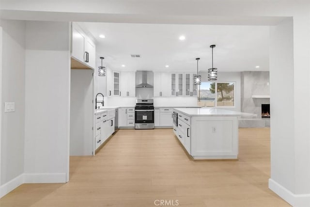 kitchen with wall chimney exhaust hood, decorative light fixtures, stainless steel range, light hardwood / wood-style floors, and white cabinets