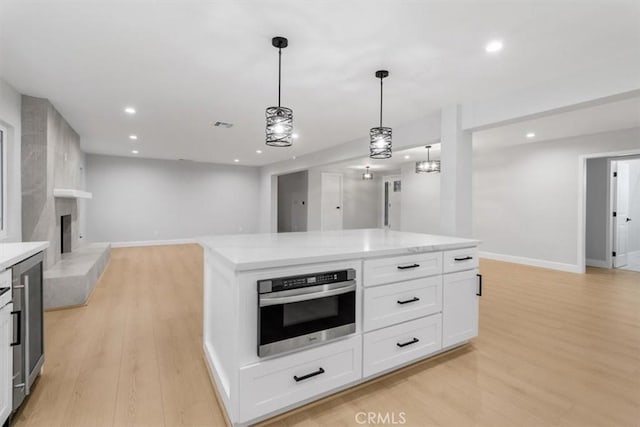 kitchen featuring hanging light fixtures, a center island, white cabinets, oven, and light wood-type flooring