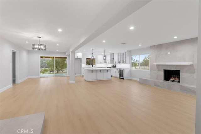 unfurnished living room with a tiled fireplace, a notable chandelier, light hardwood / wood-style floors, and beverage cooler