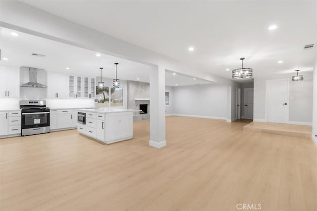 kitchen with decorative light fixtures, white cabinetry, stainless steel range, light wood-type flooring, and wall chimney exhaust hood