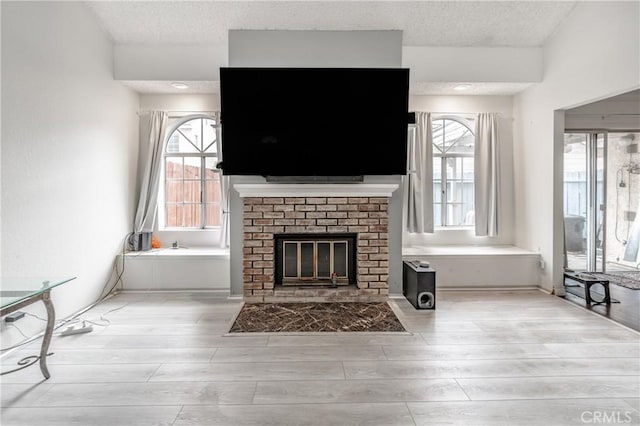 unfurnished living room with plenty of natural light, a fireplace, a textured ceiling, and light wood-style floors