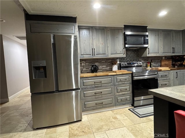 kitchen featuring stone tile flooring, decorative backsplash, gray cabinetry, butcher block countertops, and stainless steel appliances