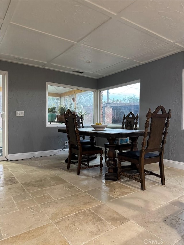 dining space with stone tile flooring, visible vents, baseboards, and a textured wall