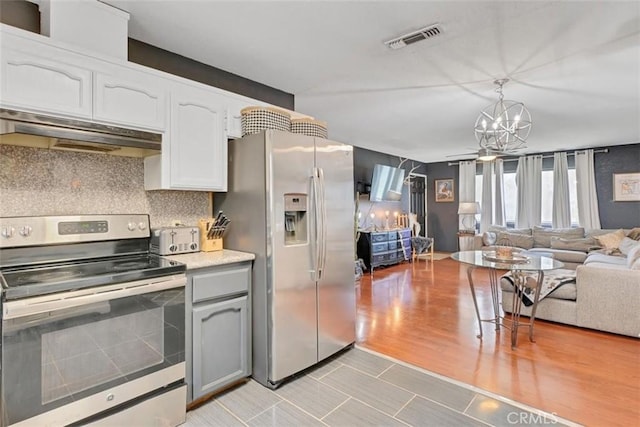 kitchen with an inviting chandelier, backsplash, appliances with stainless steel finishes, white cabinets, and pendant lighting