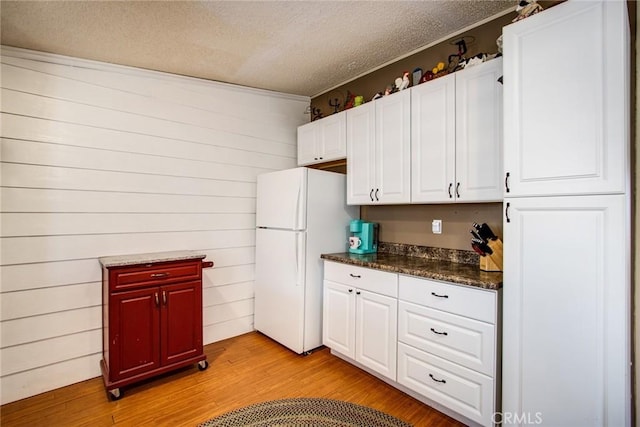 kitchen with white cabinetry, wood walls, white fridge, a textured ceiling, and light wood-type flooring