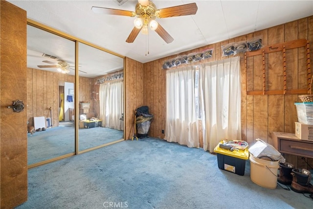 misc room featuring ceiling fan, wooden walls, a healthy amount of sunlight, and carpet flooring