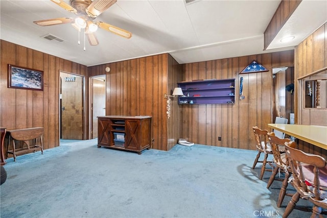 interior space with ceiling fan, wooden walls, and light carpet