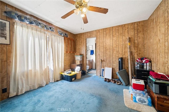 misc room featuring ceiling fan, wooden walls, and carpet flooring