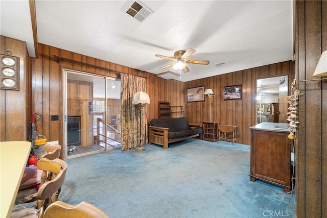 sitting room featuring carpet floors, wooden walls, and ceiling fan