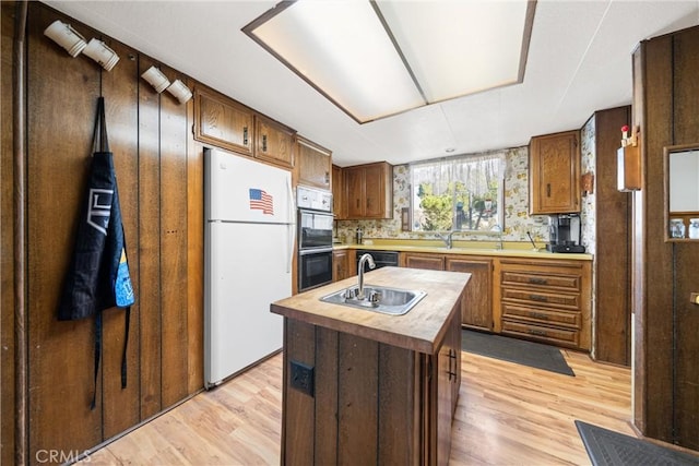 kitchen featuring white refrigerator, multiple ovens, a center island with sink, and light wood-type flooring