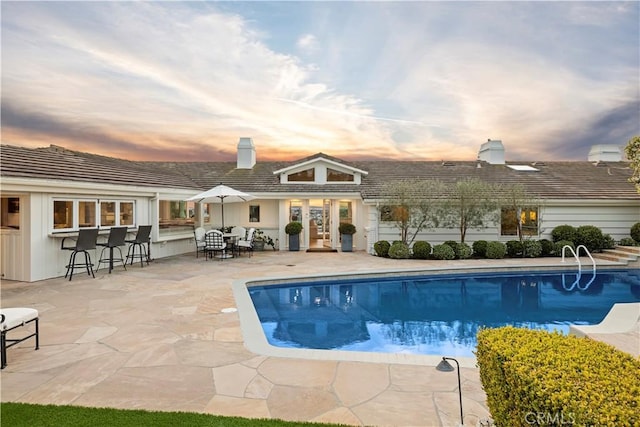 pool at dusk with an outdoor bar and a patio area