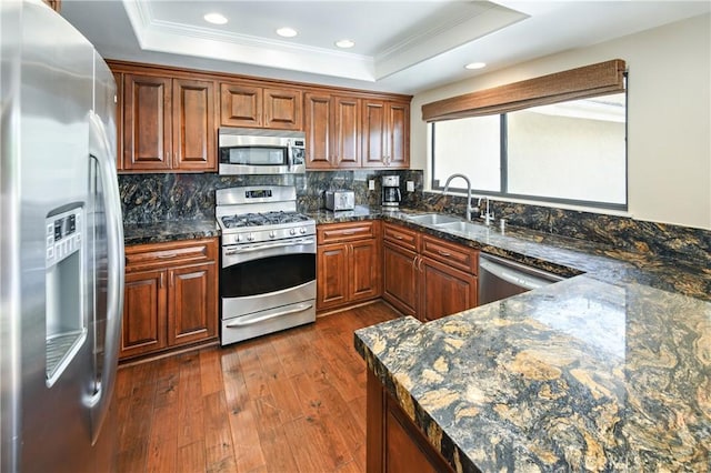 kitchen with dark stone countertops, sink, stainless steel appliances, and a raised ceiling