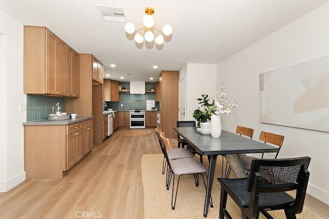 dining space with an inviting chandelier, sink, and light hardwood / wood-style floors