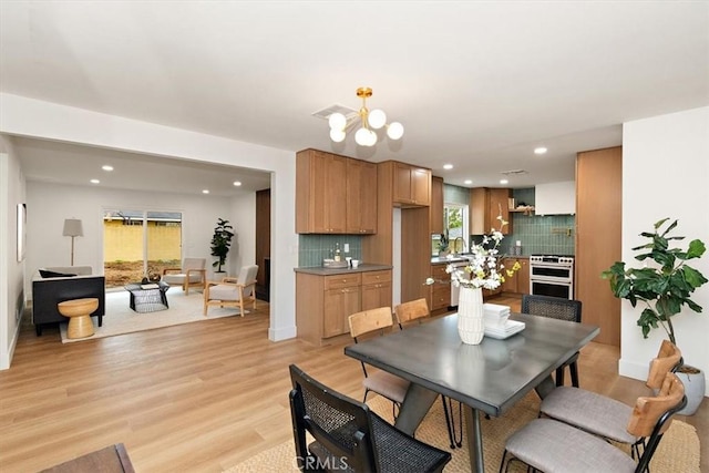 dining area with a healthy amount of sunlight, sink, a chandelier, and light hardwood / wood-style floors