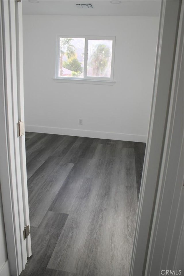 empty room with visible vents, baseboards, and dark wood-style flooring