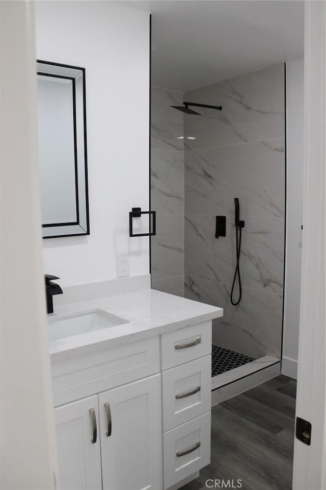 full bath with vanity, a marble finish shower, and wood finished floors