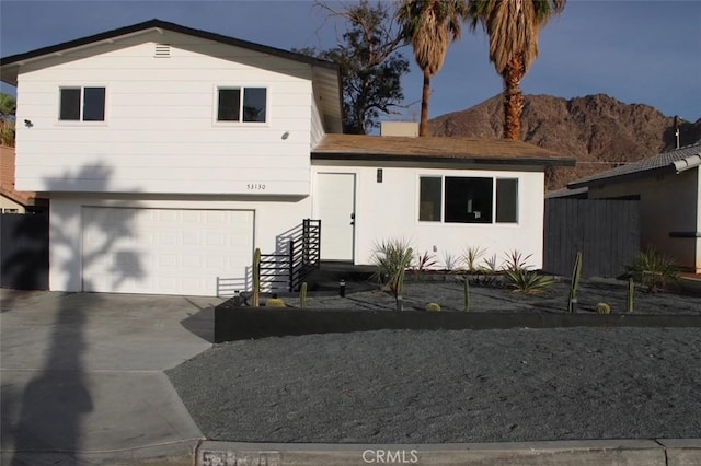 view of front facade featuring a mountain view, a garage, fence, driveway, and stucco siding