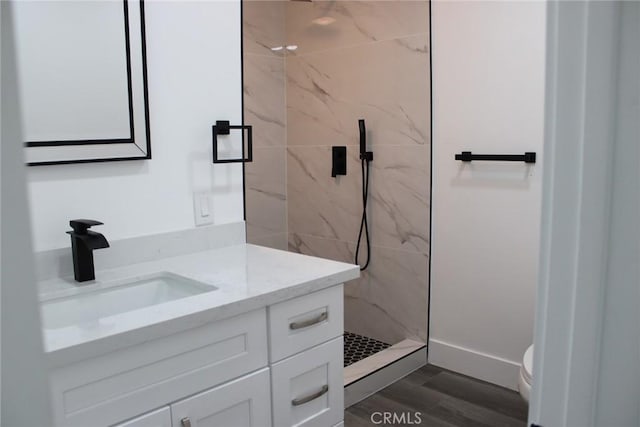 bathroom featuring toilet, wood finished floors, vanity, baseboards, and a marble finish shower