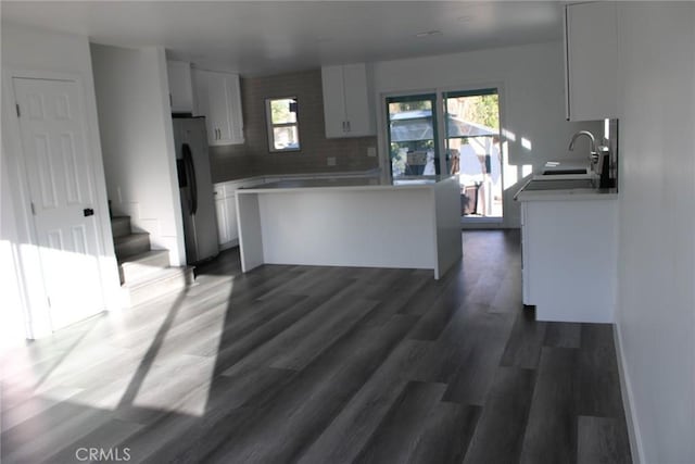 kitchen with dark wood finished floors, stainless steel refrigerator with ice dispenser, tasteful backsplash, white cabinets, and a sink