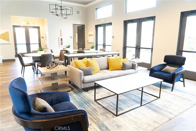 living room featuring french doors, a towering ceiling, plenty of natural light, and light wood-type flooring