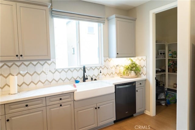 kitchen with tasteful backsplash, dishwasher, sink, and light hardwood / wood-style flooring