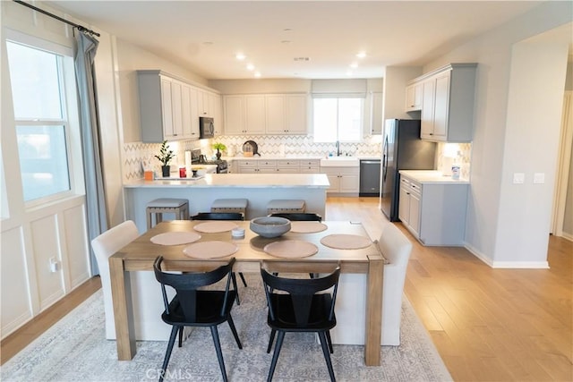 kitchen with gray cabinets, kitchen peninsula, stainless steel appliances, light hardwood / wood-style floors, and backsplash