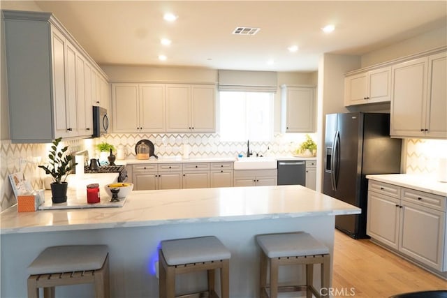 kitchen featuring sink, gray cabinetry, light wood-type flooring, a kitchen breakfast bar, and black appliances