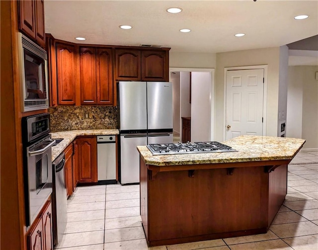 kitchen featuring light tile patterned flooring, appliances with stainless steel finishes, backsplash, and a center island