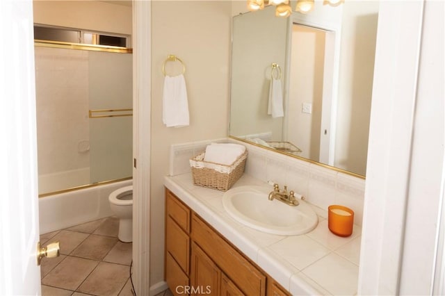 bathroom with tasteful backsplash, toilet, tile patterned floors, combined bath / shower with glass door, and vanity