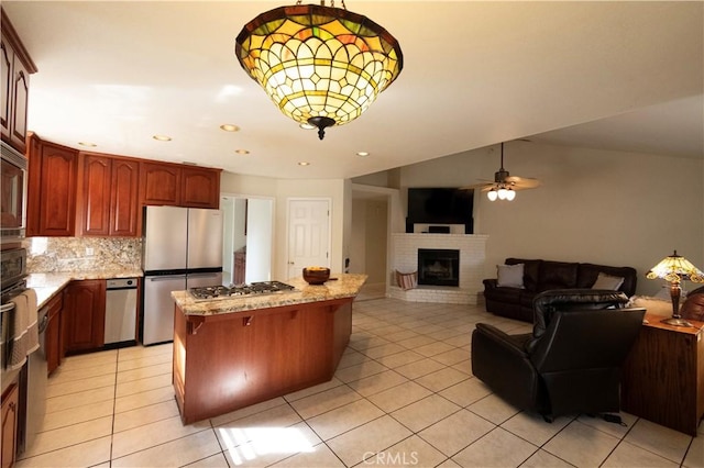 kitchen featuring decorative backsplash, appliances with stainless steel finishes, open floor plan, a brick fireplace, and light tile patterned flooring