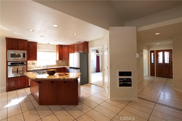 kitchen featuring light tile patterned floors, backsplash, appliances with stainless steel finishes, a kitchen island, and light stone countertops