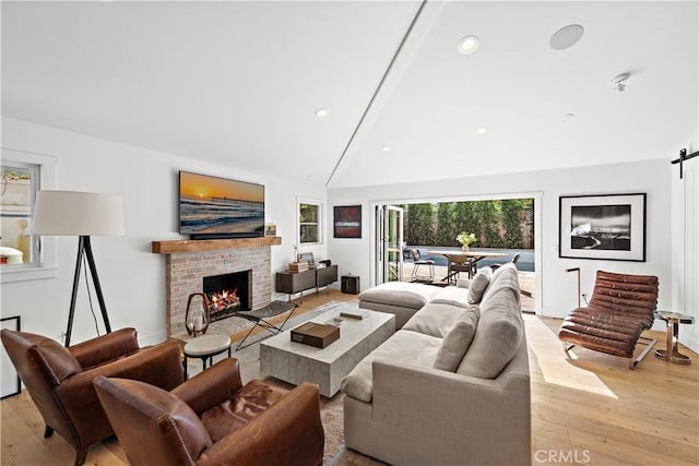 living room with a brick fireplace, high vaulted ceiling, and light wood-type flooring