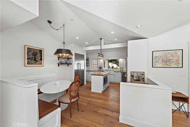 kitchen featuring vaulted ceiling, hanging light fixtures, kitchen peninsula, stainless steel appliances, and white cabinets