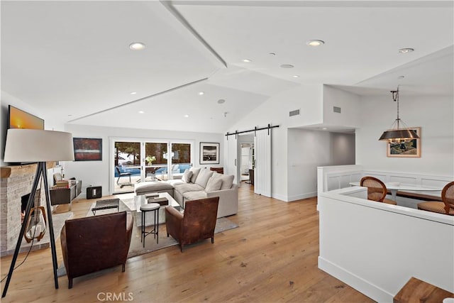 living room featuring light hardwood / wood-style flooring, a fireplace, vaulted ceiling, and a barn door