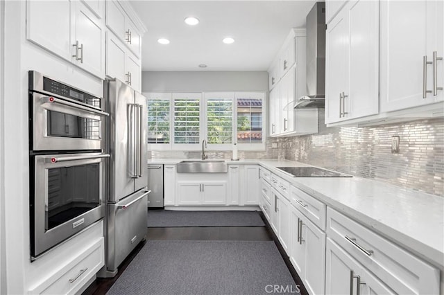 kitchen with wall chimney range hood, decorative backsplash, stainless steel appliances, white cabinetry, and a sink