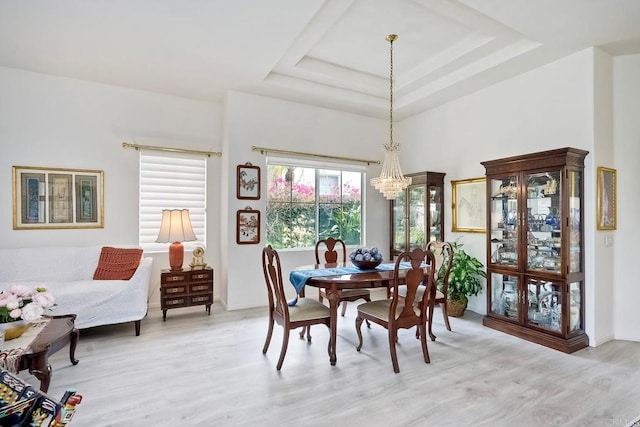 dining room featuring a notable chandelier, a raised ceiling, and light wood-type flooring