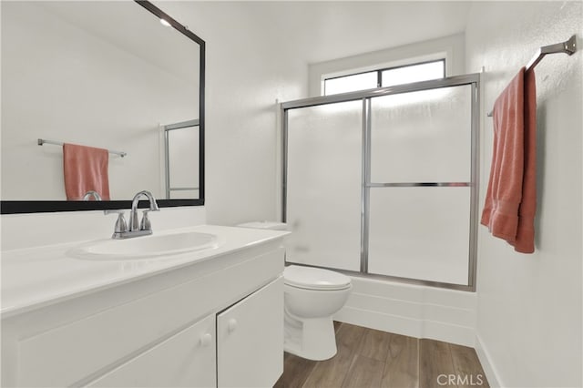 full bathroom featuring vanity, hardwood / wood-style floors, bath / shower combo with glass door, and toilet