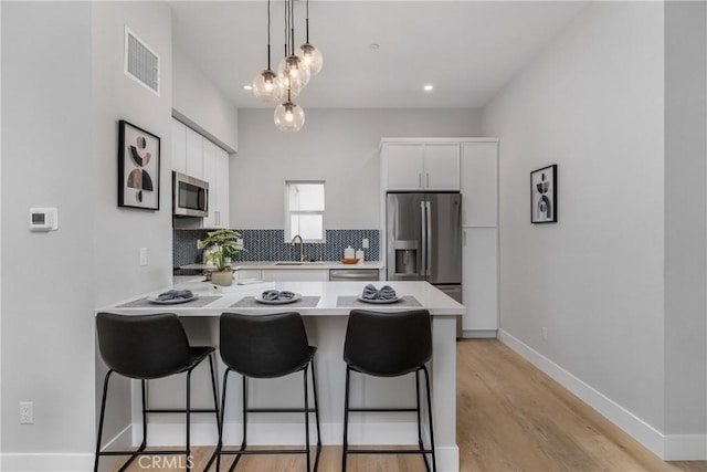 kitchen with pendant lighting, appliances with stainless steel finishes, backsplash, a kitchen breakfast bar, and white cabinets