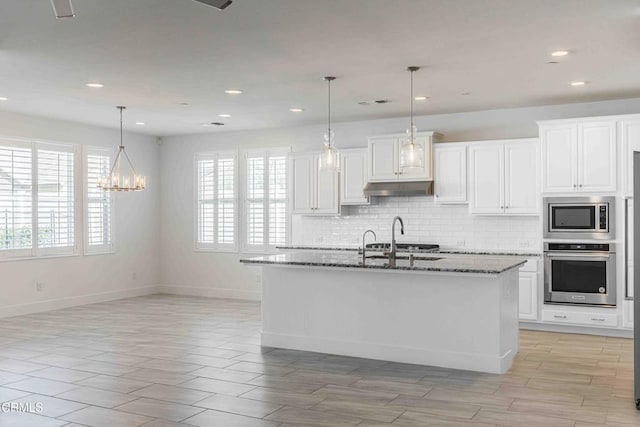 14706 Pemberley Passage Ave, Bakersfield, CA 93311 - kitchen featuring dark stone countertops, appliances with stainless steel finishes, an island with sink, pendant lighting, and white cabinets