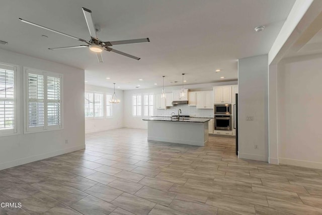 14706 Pemberley Passage Ave, Bakersfield, CA 93311 - kitchen featuring appliances with stainless steel finishes, decorative light fixtures, tasteful backsplash, an island with sink, and white cabinets