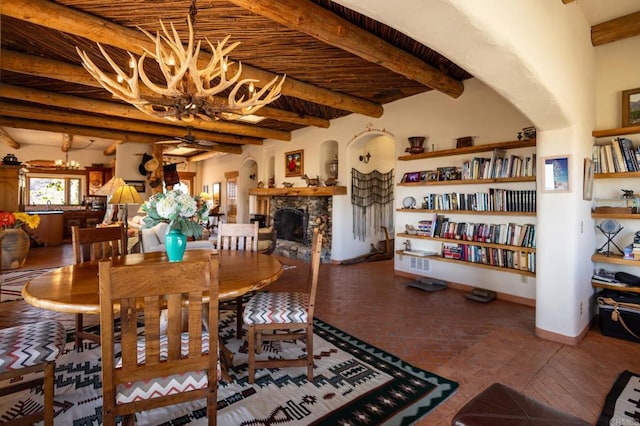 dining room with arched walkways, brick floor, a fireplace, beam ceiling, and ceiling fan with notable chandelier