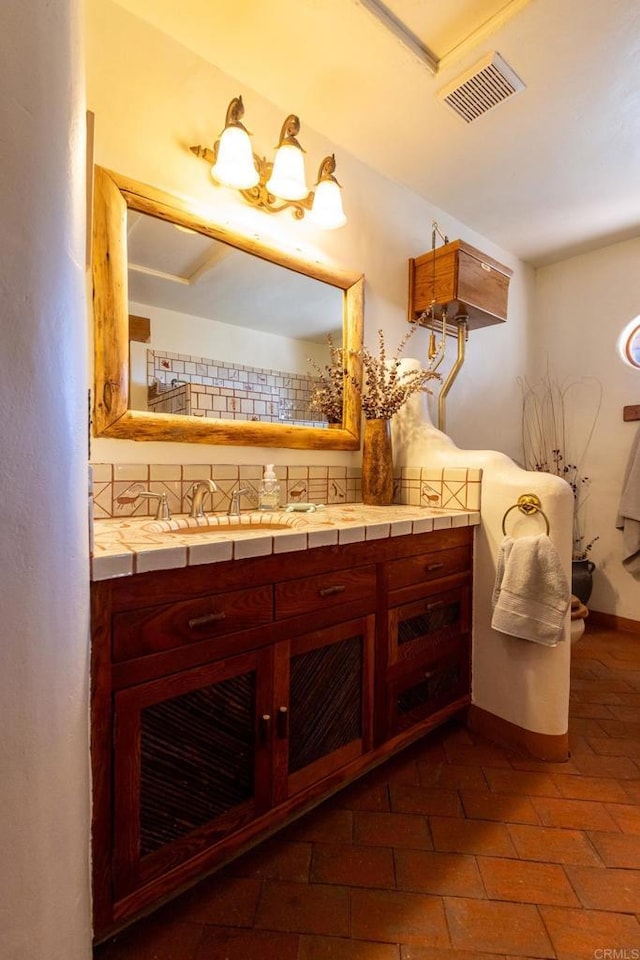 bathroom with brick floor, visible vents, backsplash, vanity, and baseboards