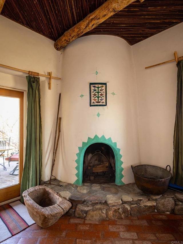 unfurnished room featuring a fireplace with raised hearth, beamed ceiling, brick floor, and wooden ceiling