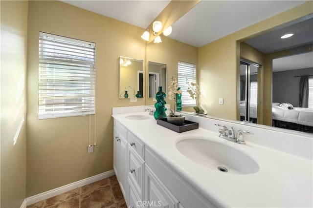 full bath featuring double vanity, ensuite bathroom, baseboards, and a sink