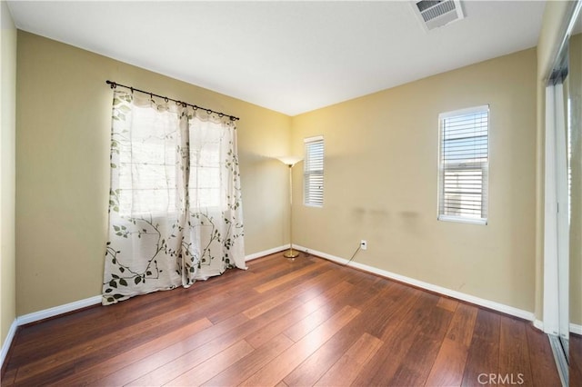 empty room featuring plenty of natural light, baseboards, visible vents, and wood-type flooring