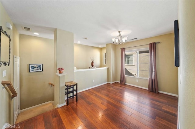 unfurnished room featuring a notable chandelier, baseboards, visible vents, and wood-type flooring