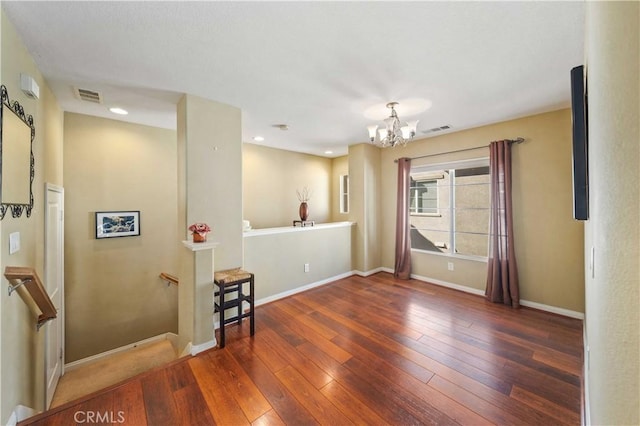 spare room featuring visible vents, baseboards, a notable chandelier, and hardwood / wood-style flooring