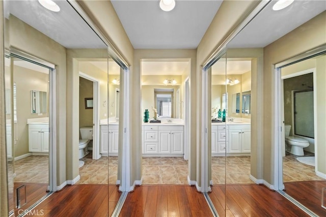 full bathroom with baseboards, toilet, two vanities, and hardwood / wood-style floors